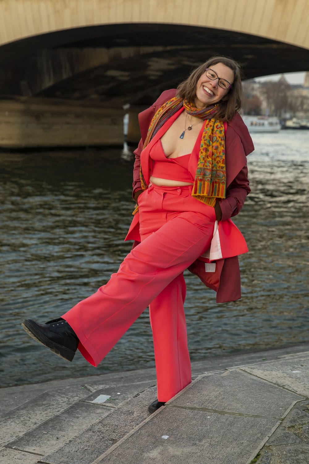 brown hair latina with light skin under a Paris bridge - Luna's a former academic (professor) of 20 years who quit academia to be a career clarity coach for mid-career lecturers, post-docs, professors who want a better life by leaving academia. Luna is in a 3 piece coral-colored suit and a huge smile while kicking the air playfully